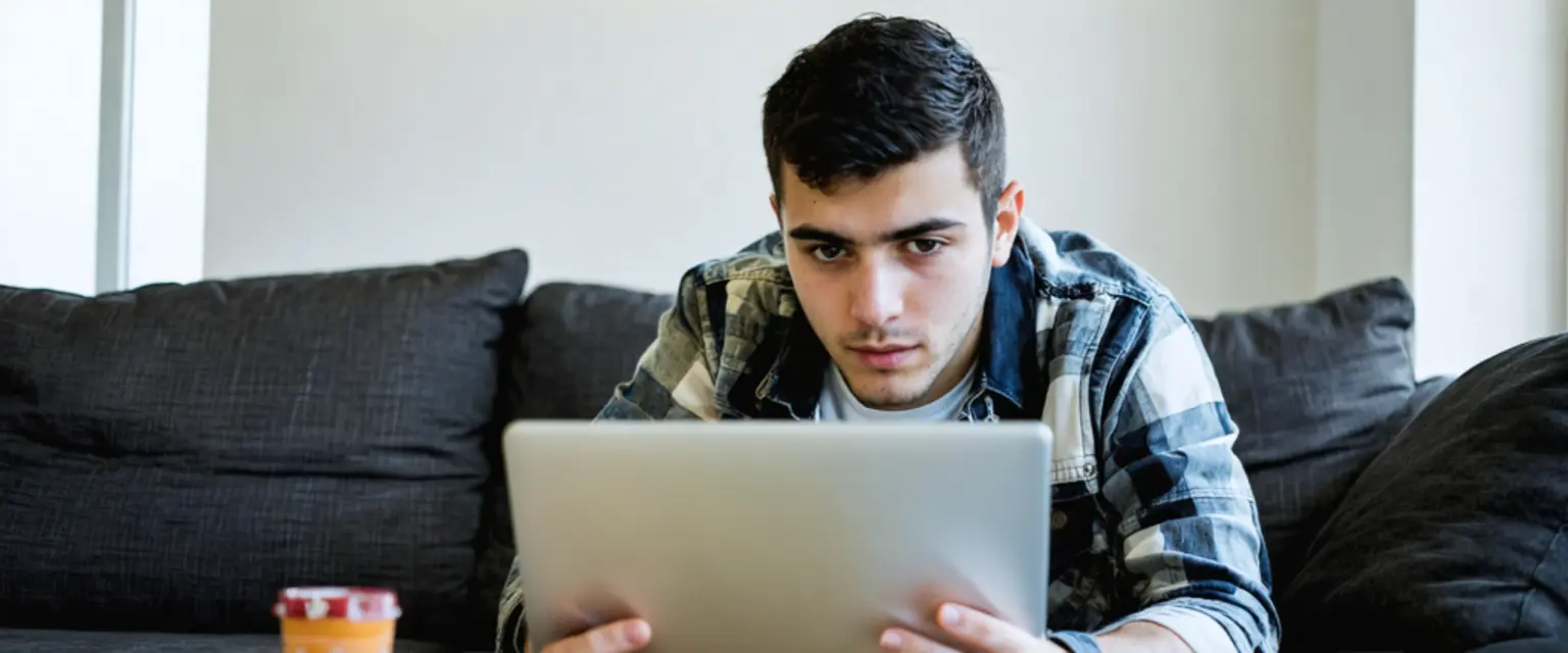 رجل يستخدم الحاسوب المحمول مع رمز درع أمان، يرمز لحماية حسابات الألعاب من الهجمات السيبرانية.